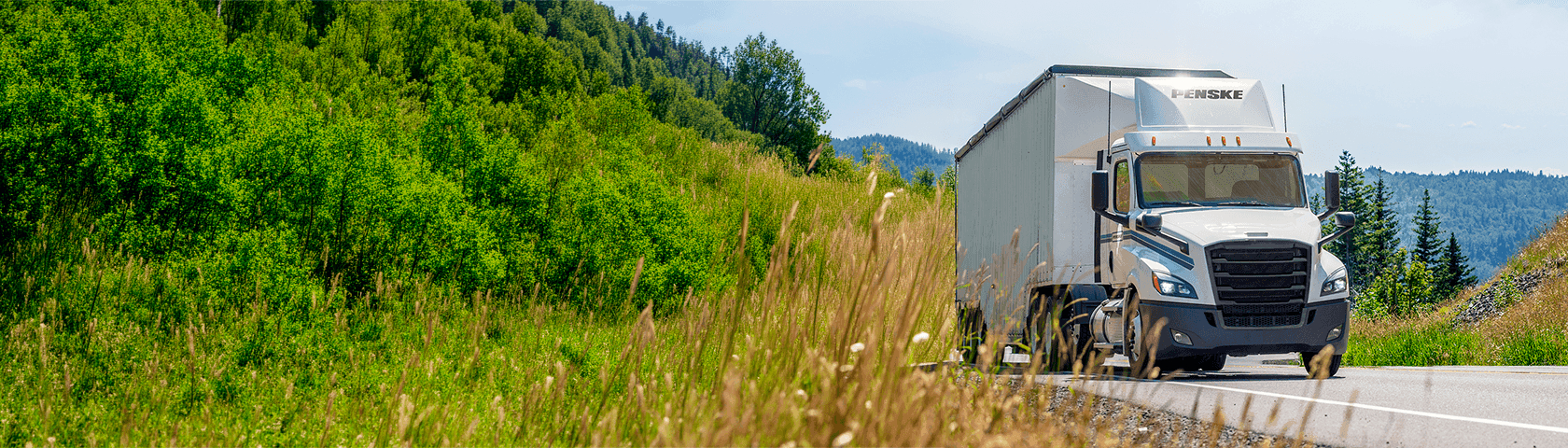 White Penske tractor trailer on a road by a hill