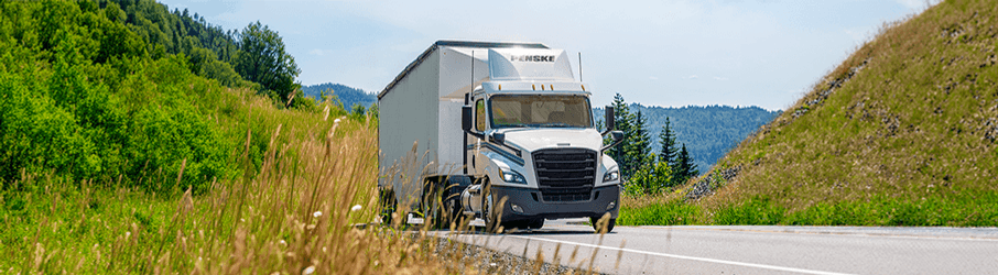 White Penske tractor trailer on a road by a hill